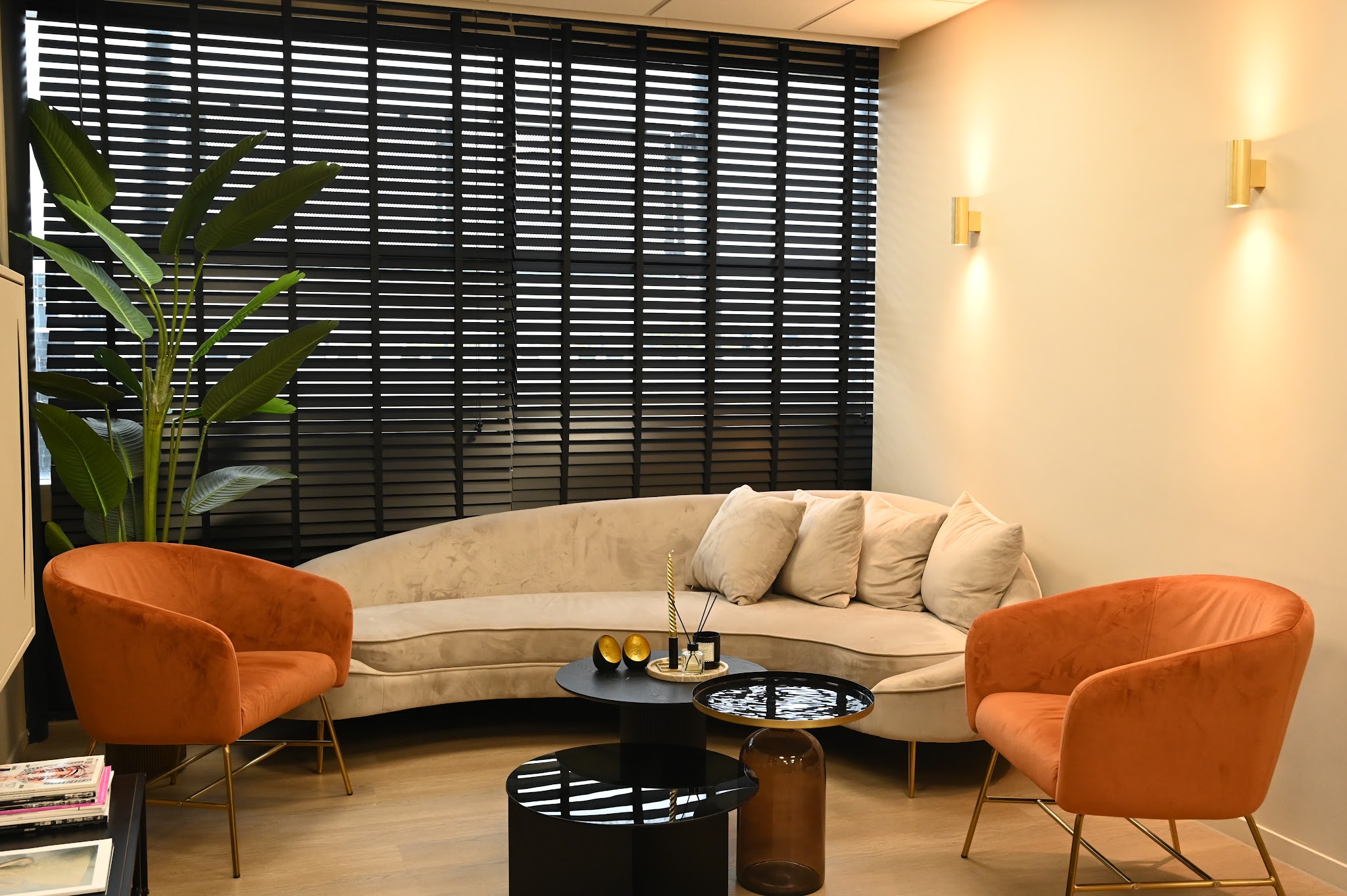De lounge met terracotta fauteuils, een ronde crèmekleurige bank en een plant