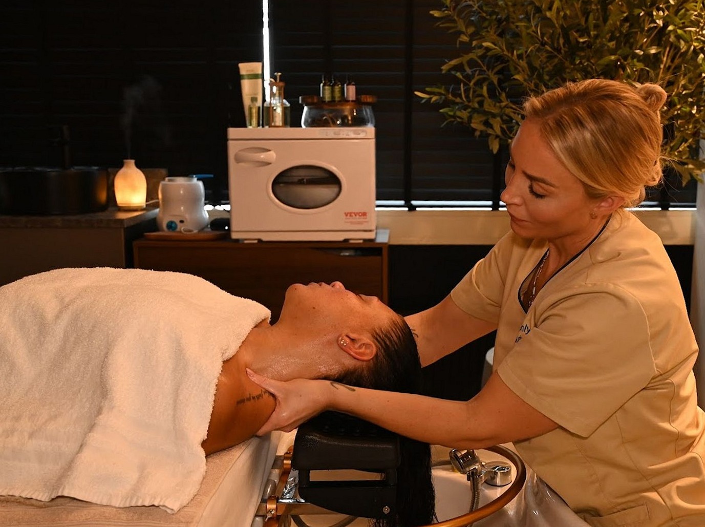Hoofd- en nekmassage boven de headspa-wasbak, de behandelaar in beige tuniek